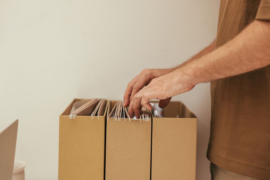A hand sorting hanging document folders packed inside a cardboard archive box ready for collection