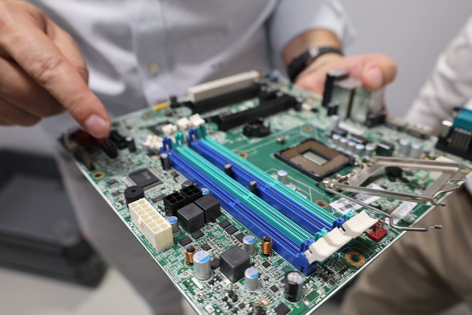 A technician's hands carefully removing a component from a computer motherboard during IT equipment dismantling
