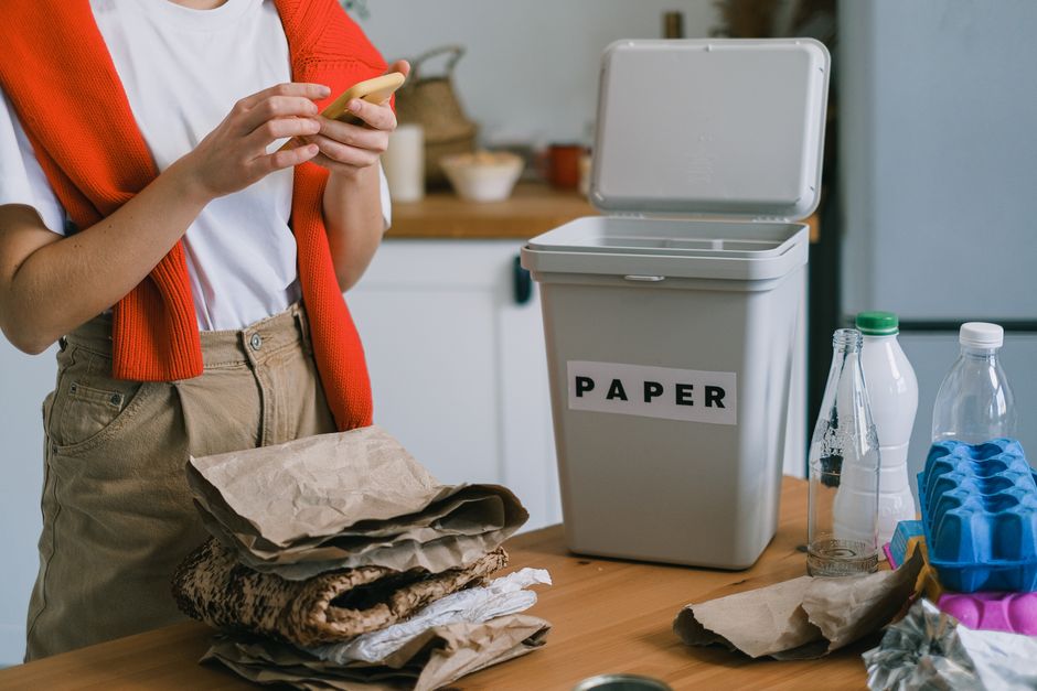 Person sorting paper recycling into a labelled paper bin alongside glass bottles and jars for recycling