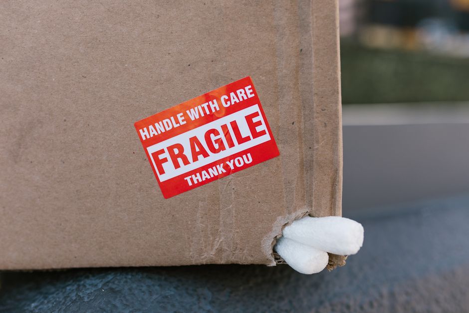 A red FRAGILE handle with care sticker on the corner of a cardboard shipping box