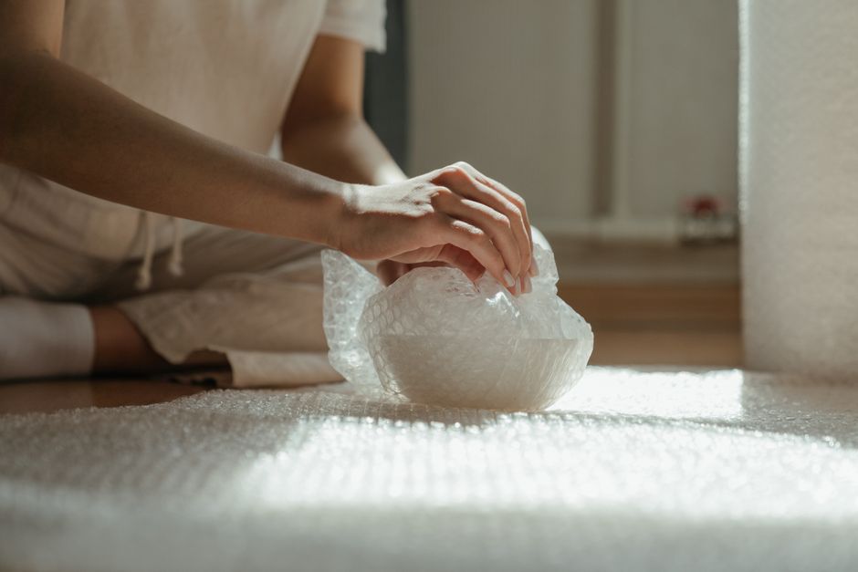 Wrapping a fragile item in bubble wrap by hand before placing it in a shipping box