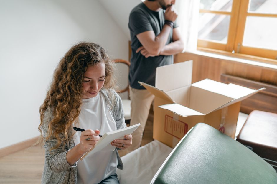 A couple sitting among moving boxes, writing a packing list while planning their move