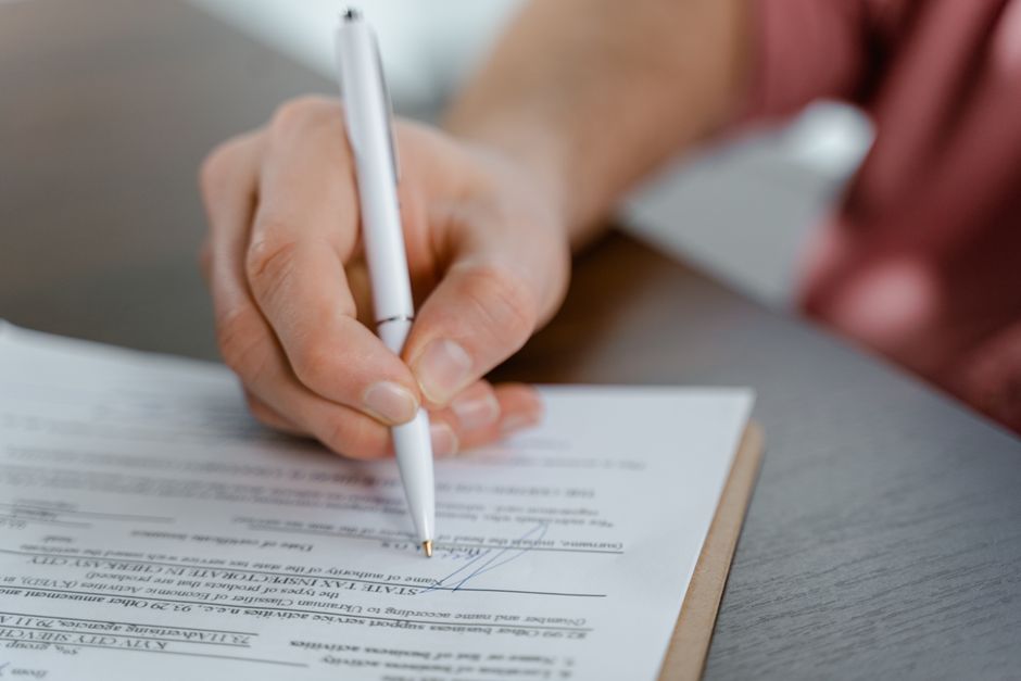 Close-up of a hand signing a printed form with a pen on a clipboard