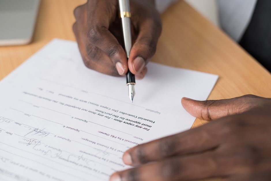 Person reviewing and writing on a paper agreement at a desk with a glass of water nearby