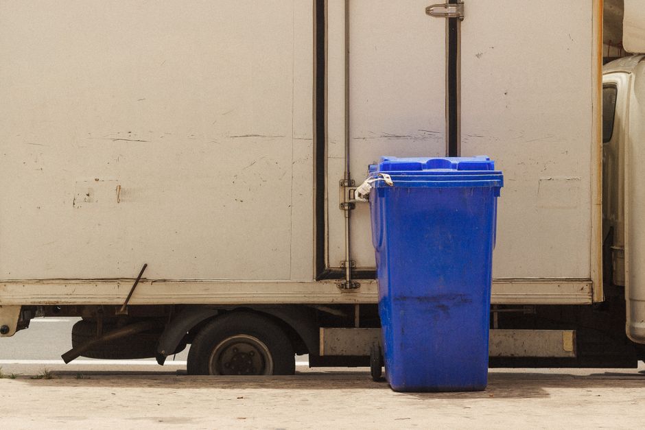 A blue wheelie recycling bin standing beside a collection van, illustrating kerbside and site recycling collection