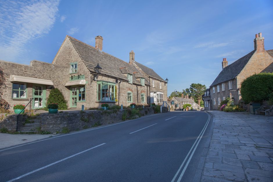 A quiet stone-built English village street lined with traditional cottages