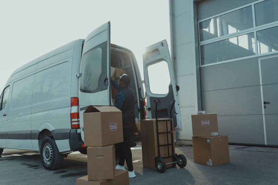 Man pulling a sack truck loaded with cardboard boxes towards a van outside a warehouse