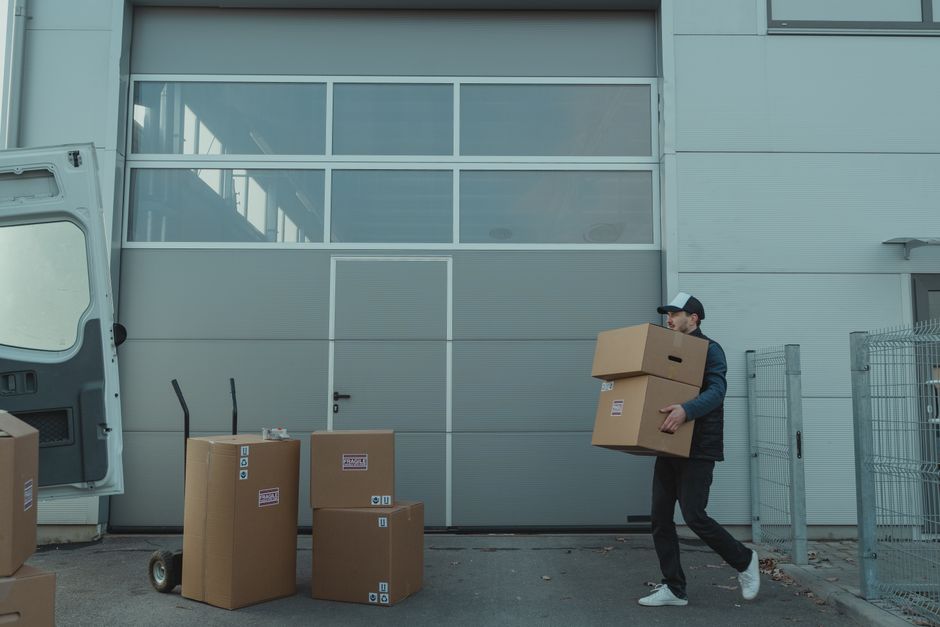 A man carrying stacked cardboard boxes out of a loading door