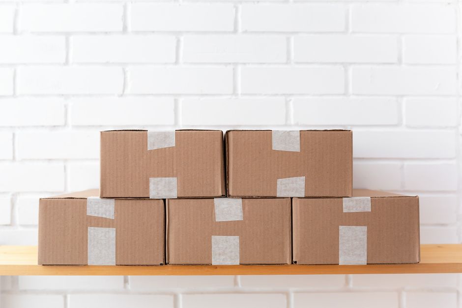 Stack of taped cardboard boxes on a wooden shelf against a brick wall