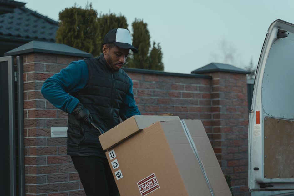 A man carrying a fragile-marked cardboard box toward an open van