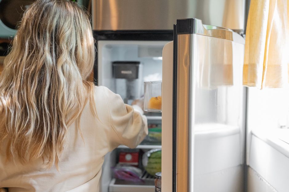 A person reaching into an open fridge to remove food items