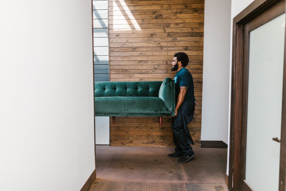 A man carrying an upholstered sofa through a doorway during a collection