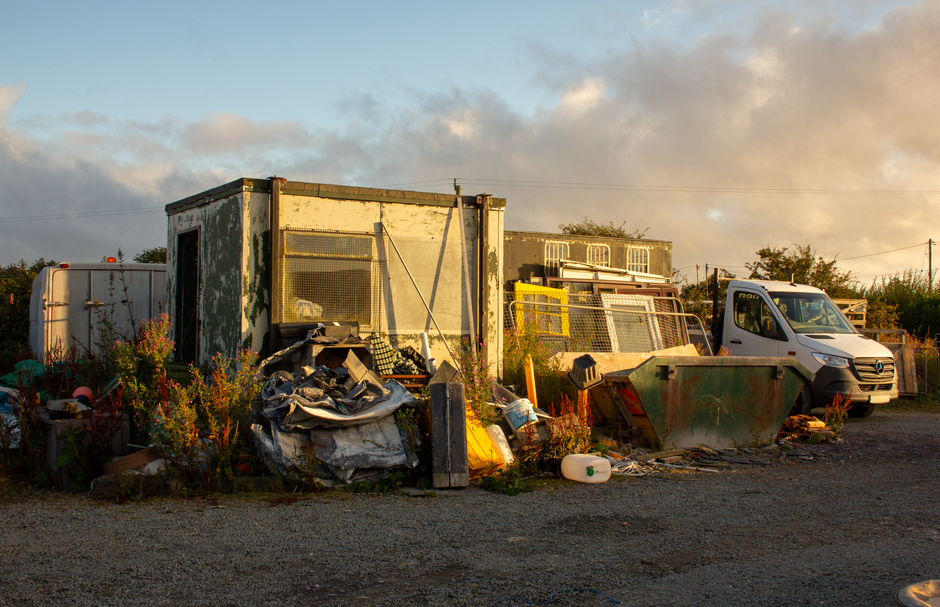 A rural household waste and skip site with a van parked beside a loaded skip