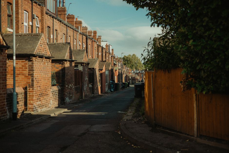 A UK back alley lined with red-brick terraced houses and wheelie bins