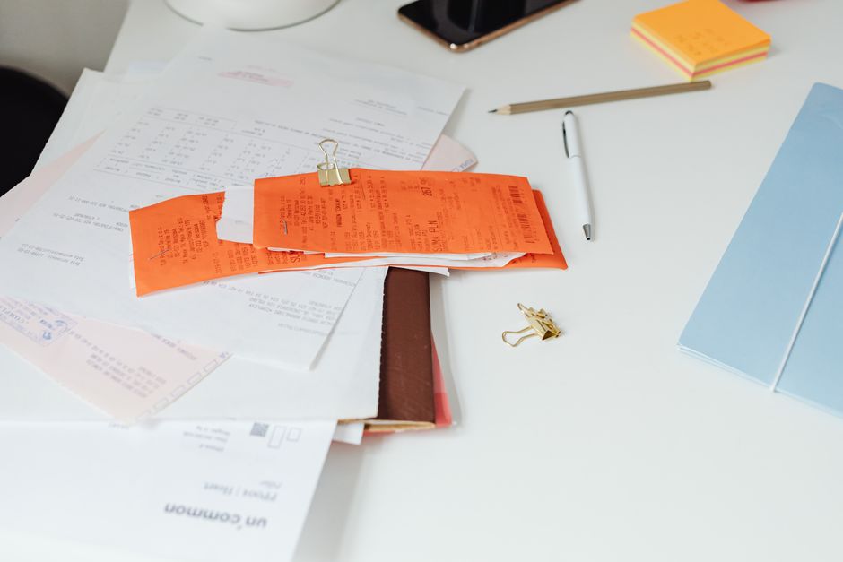 A pile of paper receipts and invoices on a desk with a pen and sticky notes