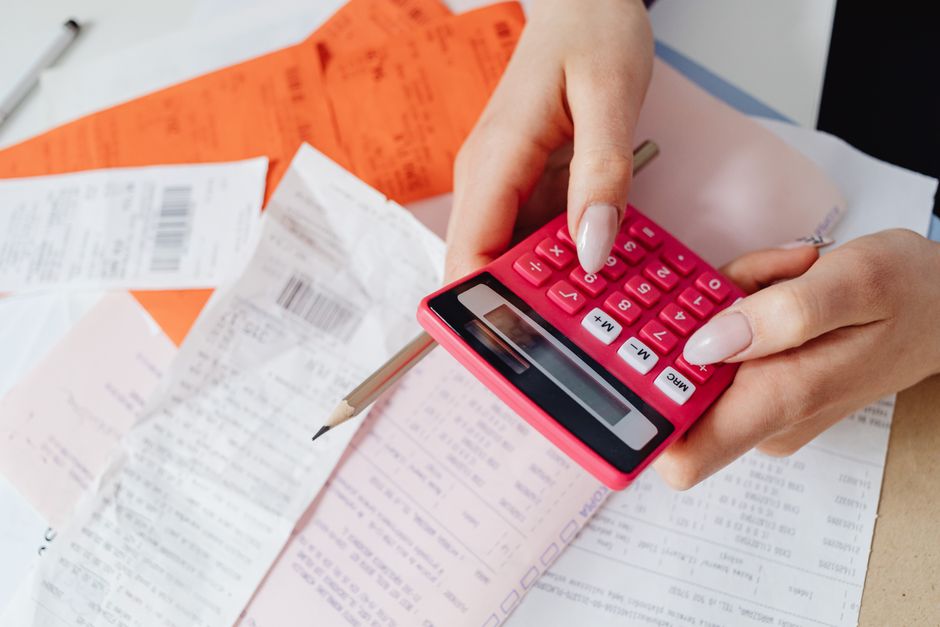 A person using a calculator while checking paper receipts spread out on a desk