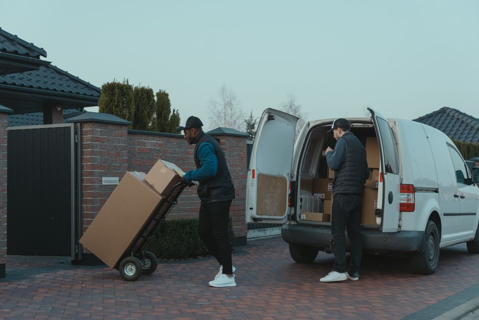 Two movers loading cardboard boxes into a van parked on a residential driveway