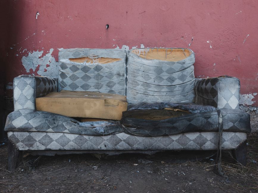 A worn, heavily used sofa left outdoors against a wall, representative of the kind of bulky item a council collection removes