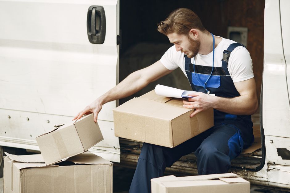 A delivery worker checking an item against paperwork at the open back doors of a van