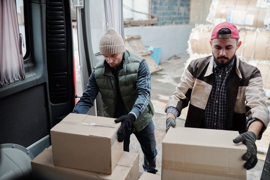 Two workers loading cardboard boxes into the back of a van during a property clearance